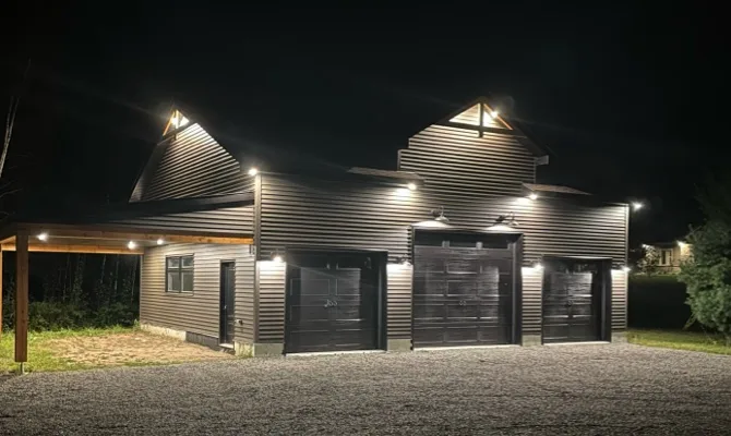Garage spacieux à trois portes avec éclairage extérieur moderne, conçu par un entrepreneur général pour un espace fonctionnel et esthétique.