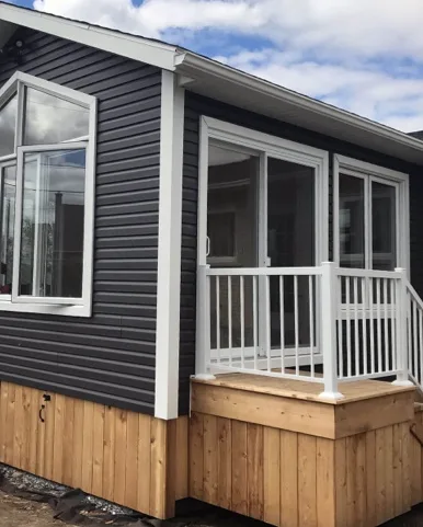 renovation-2017-10-agrandissement-quatre-saisons-16 Façade de maison moderne avec revêtement noir, accents en bois et balcon blanc, réalisée par un entrepreneur général spécialisé en construction résidentielle.